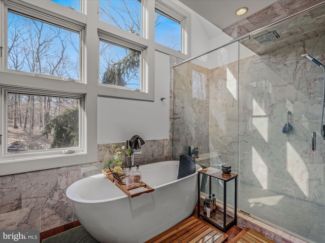 bathroom featuring tile walls, a marble finish shower, a soaking tub, a towering ceiling, and wainscoting