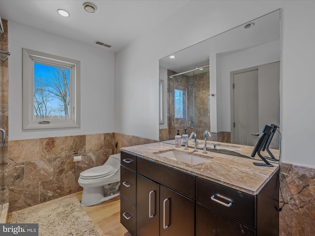 bathroom featuring toilet, a wainscoted wall, visible vents, tile walls, and a shower stall