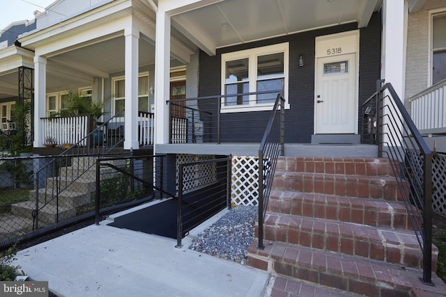 property entrance featuring covered porch, fence, and brick siding