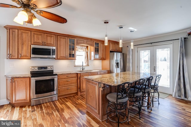 kitchen with brown cabinets, appliances with stainless steel finishes, a healthy amount of sunlight, a sink, and wood finished floors