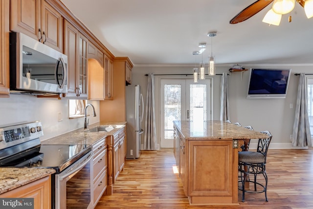 kitchen with a breakfast bar area, stainless steel appliances, a kitchen island, a sink, and light stone countertops