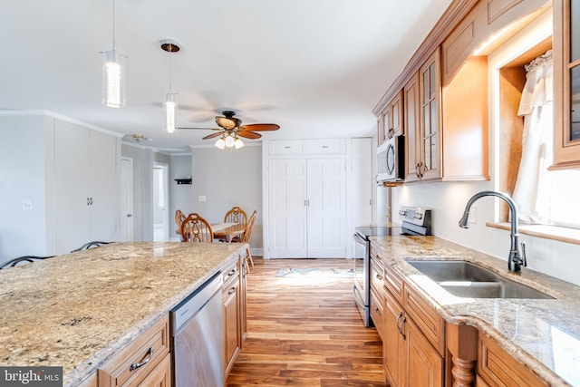 kitchen featuring light stone counters, light wood finished floors, stainless steel appliances, hanging light fixtures, and a sink