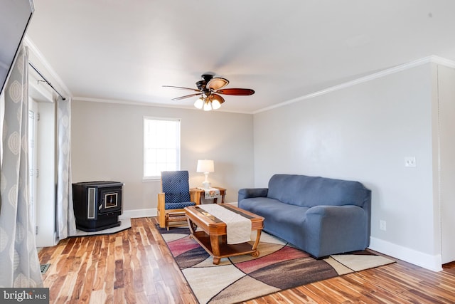 living room featuring baseboards, light wood finished floors, a wood stove, and crown molding