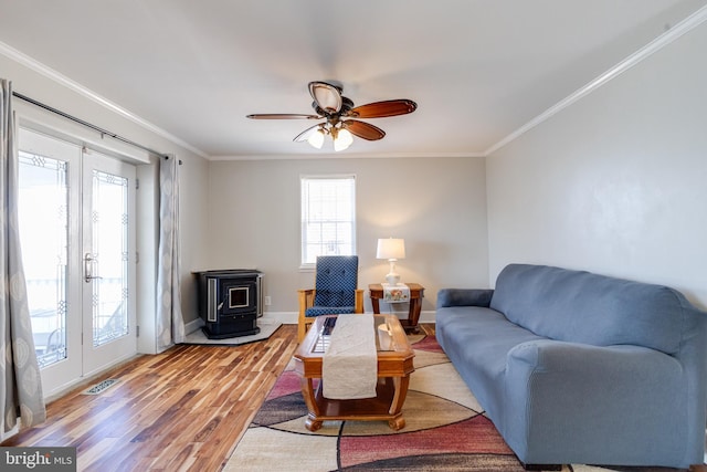 living room with a wood stove, ornamental molding, light wood-style flooring, and baseboards