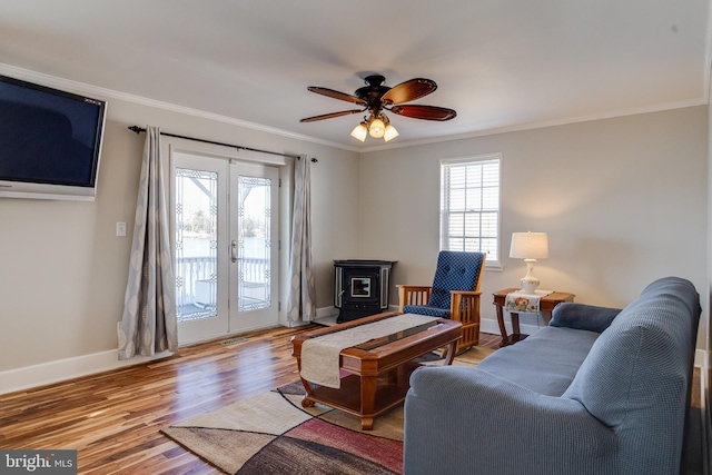 living area with baseboards, a ceiling fan, wood finished floors, a wood stove, and crown molding