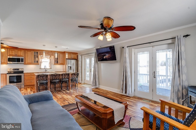 living area featuring baseboards, french doors, light wood-type flooring, and crown molding