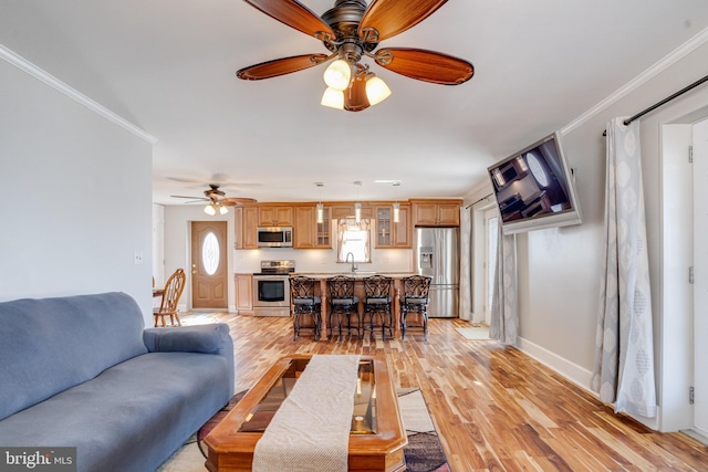 living area featuring ceiling fan, ornamental molding, light wood-style flooring, and baseboards