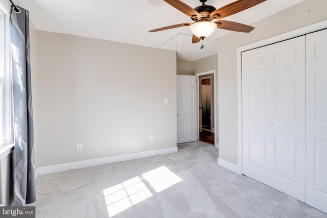 unfurnished bedroom with a closet, light carpet, ceiling fan, and baseboards