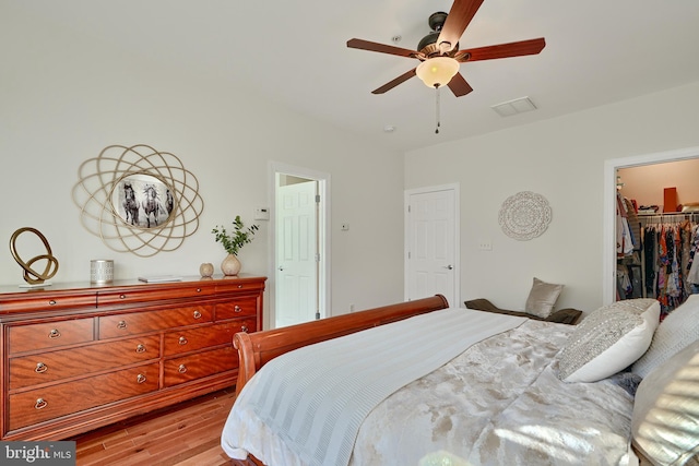 bedroom featuring a spacious closet, a closet, a ceiling fan, and light wood-style floors