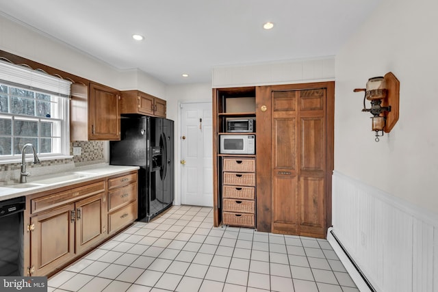 kitchen featuring light countertops, baseboard heating, wainscoting, black appliances, and a sink