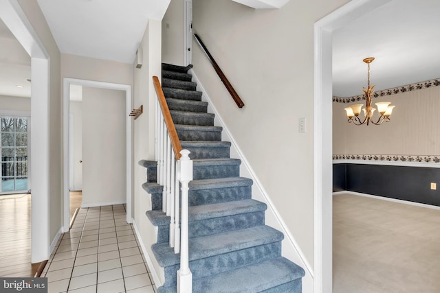 staircase with an inviting chandelier, baseboards, and tile patterned floors