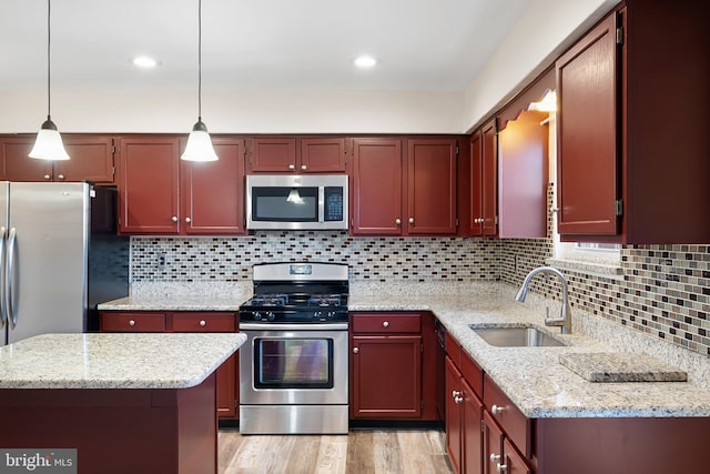 kitchen with a sink, appliances with stainless steel finishes, light wood-type flooring, tasteful backsplash, and pendant lighting