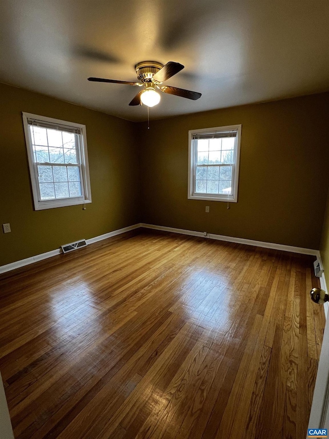 empty room with a ceiling fan, wood finished floors, visible vents, and baseboards