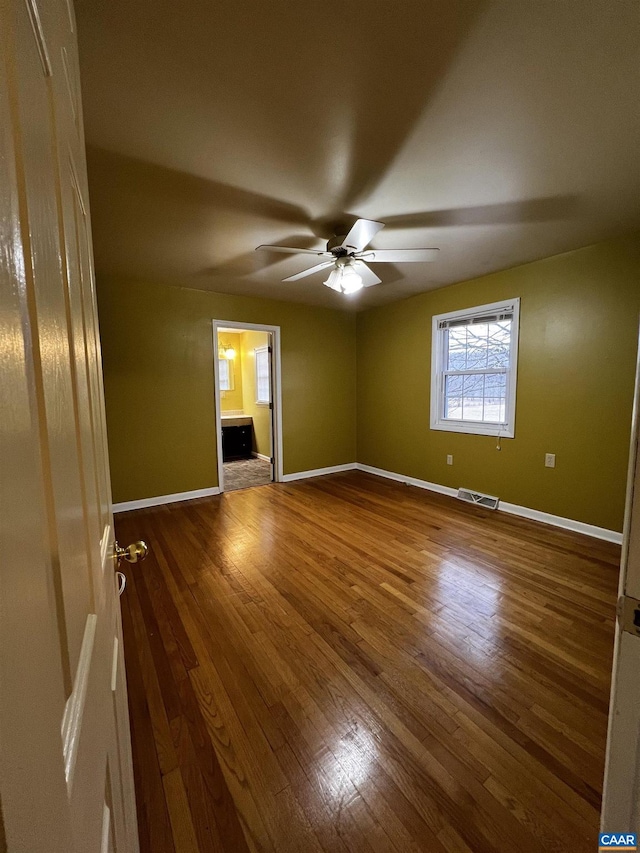 empty room featuring a ceiling fan, wood finished floors, visible vents, and baseboards