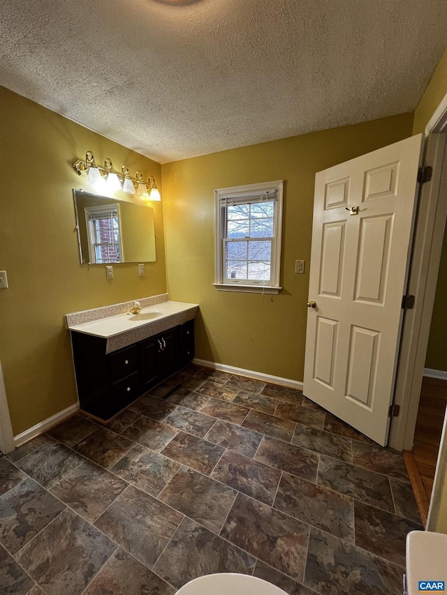 bathroom featuring stone finish floor, vanity, baseboards, and a textured ceiling