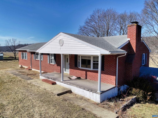 view of front facade featuring roof with shingles, brick siding, and a chimney