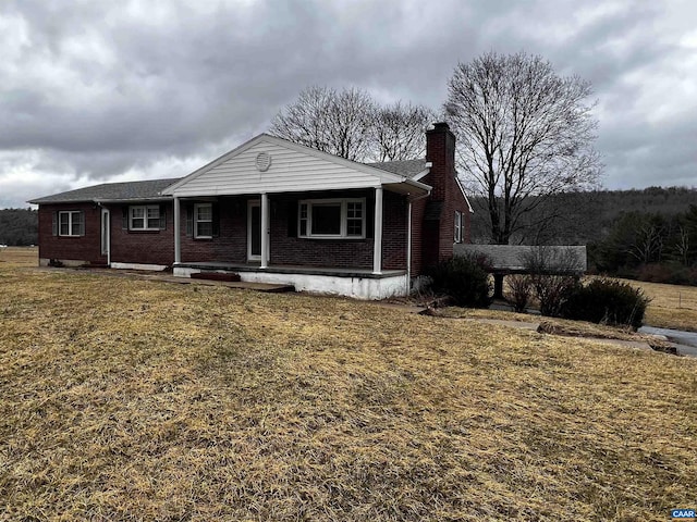 view of front facade featuring covered porch, brick siding, a chimney, and a front yard