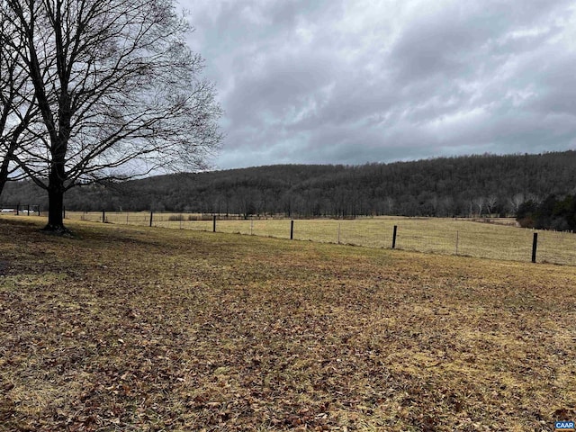 view of yard featuring a wooded view, a rural view, and fence