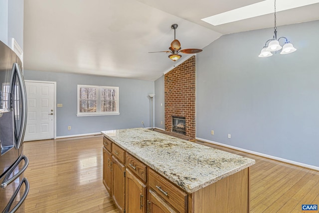 kitchen featuring light wood-style floors, lofted ceiling with skylight, a brick fireplace, ceiling fan, and stainless steel fridge