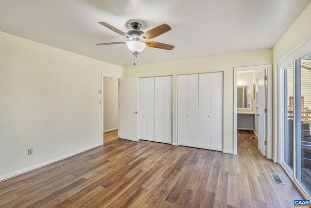 unfurnished bedroom with baseboards, visible vents, two closets, and wood finished floors