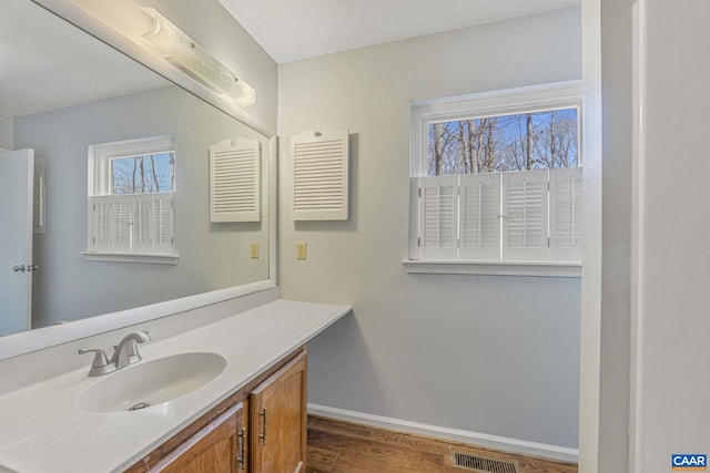 bathroom with visible vents, vanity, baseboards, and wood finished floors