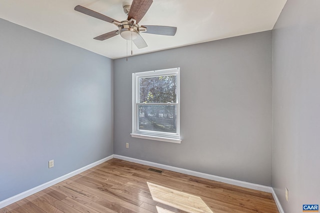 empty room featuring hardwood / wood-style floors, a ceiling fan, visible vents, and baseboards