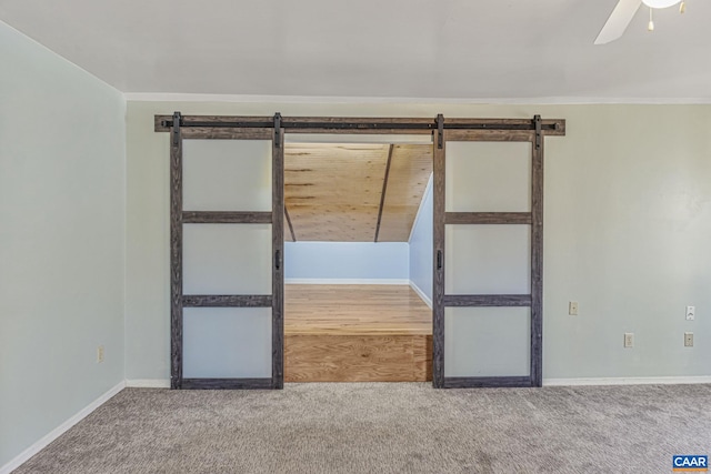 spare room featuring ceiling fan, a barn door, carpet floors, baseboards, and crown molding