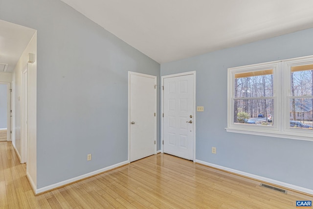 empty room with attic access, baseboards, visible vents, wood finished floors, and vaulted ceiling