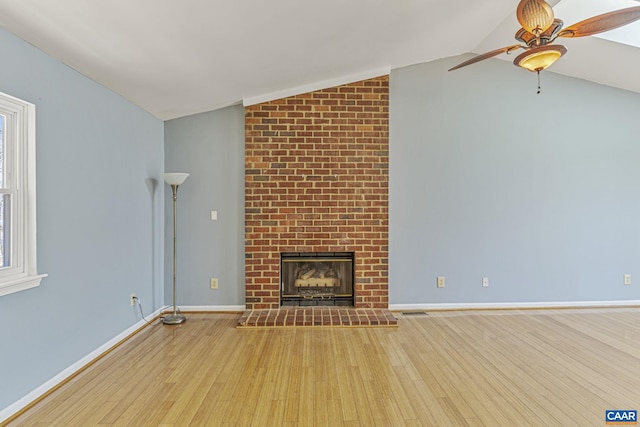 unfurnished living room featuring lofted ceiling, a brick fireplace, a wealth of natural light, and wood finished floors