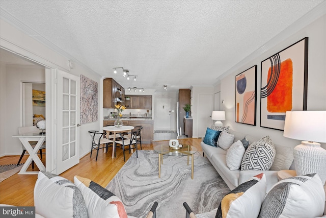 living area with light wood-type flooring, ornamental molding, a textured ceiling, and french doors