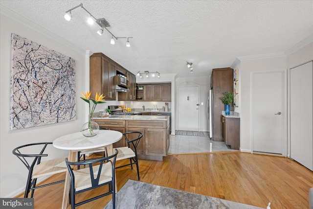 kitchen featuring light wood-style flooring, stainless steel appliances, a textured ceiling, light countertops, and crown molding