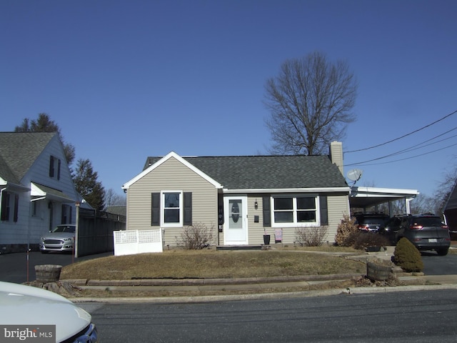 view of front of house featuring driveway, an attached carport, a chimney, and a shingled roof