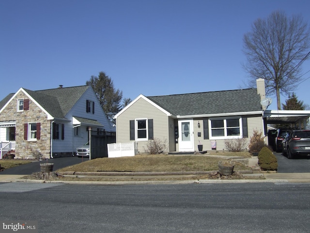 view of front facade featuring a shingled roof, stone siding, driveway, a carport, and a chimney