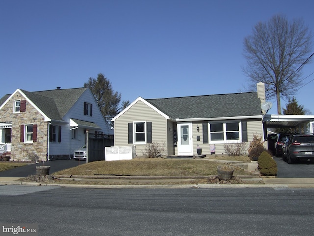 view of front of home with driveway, a shingled roof, a chimney, and a carport