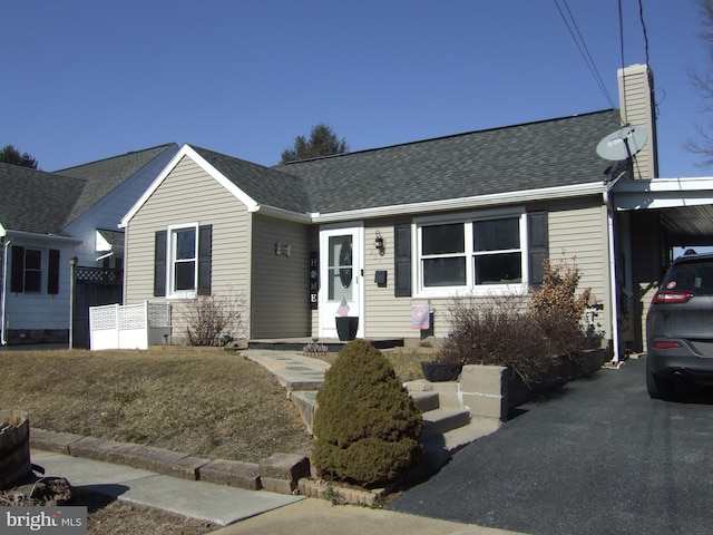 ranch-style home featuring a shingled roof, an attached carport, driveway, and a chimney