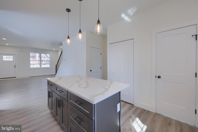 kitchen featuring pendant lighting, light wood finished floors, a kitchen island, light stone countertops, and baseboards