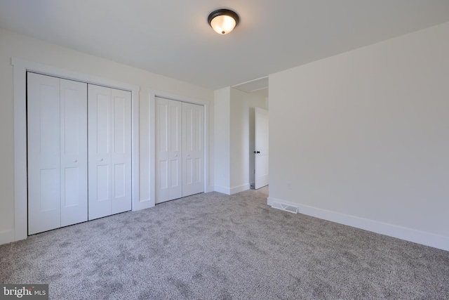 unfurnished bedroom featuring baseboards, carpet, visible vents, and multiple closets