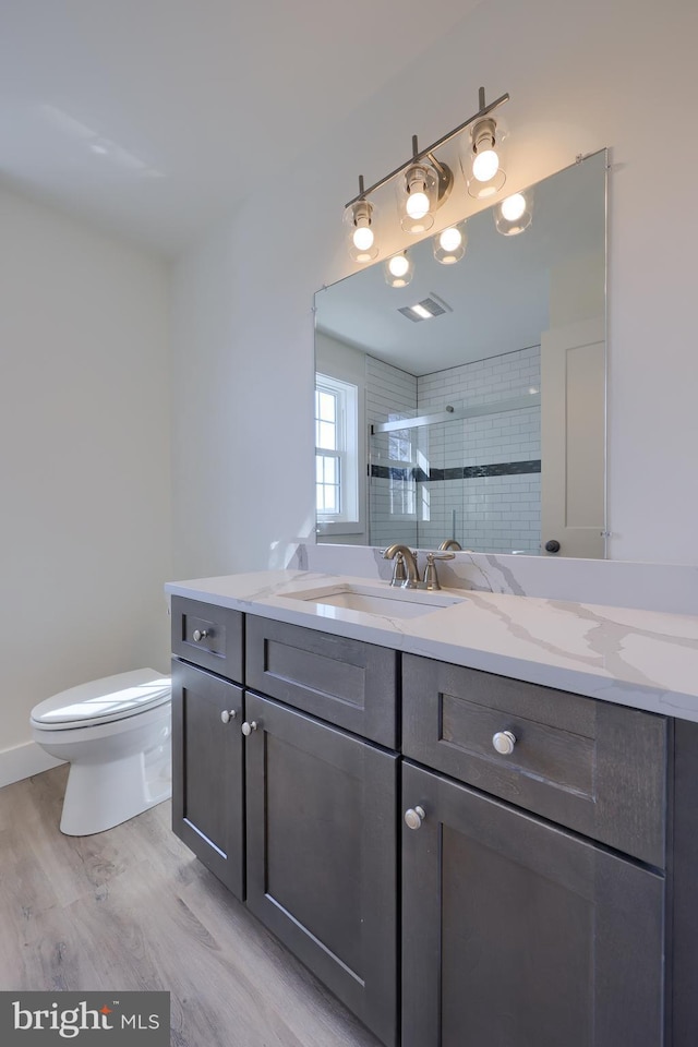 bathroom featuring visible vents, toilet, wood finished floors, vanity, and a shower stall