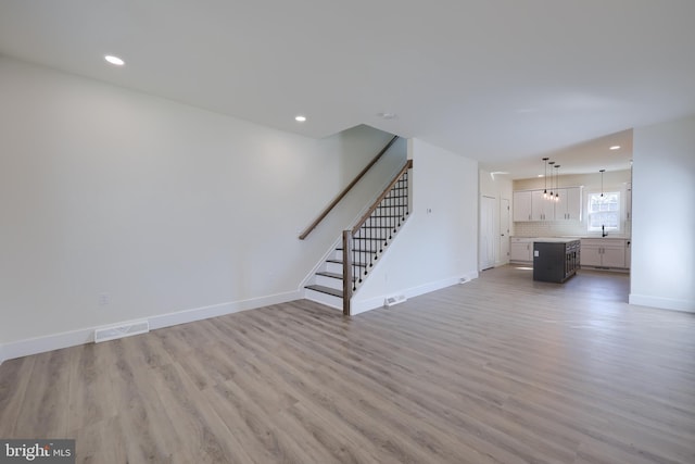 unfurnished living room with recessed lighting, visible vents, stairway, light wood-type flooring, and baseboards