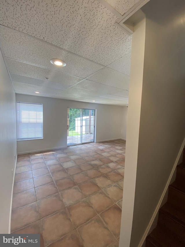 empty room featuring a paneled ceiling, a healthy amount of sunlight, stairway, and baseboards