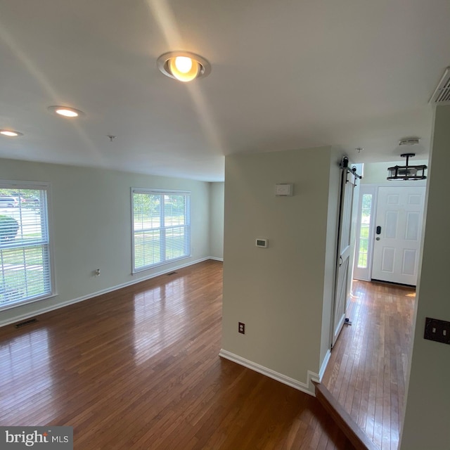 empty room featuring a healthy amount of sunlight, a barn door, visible vents, and wood finished floors
