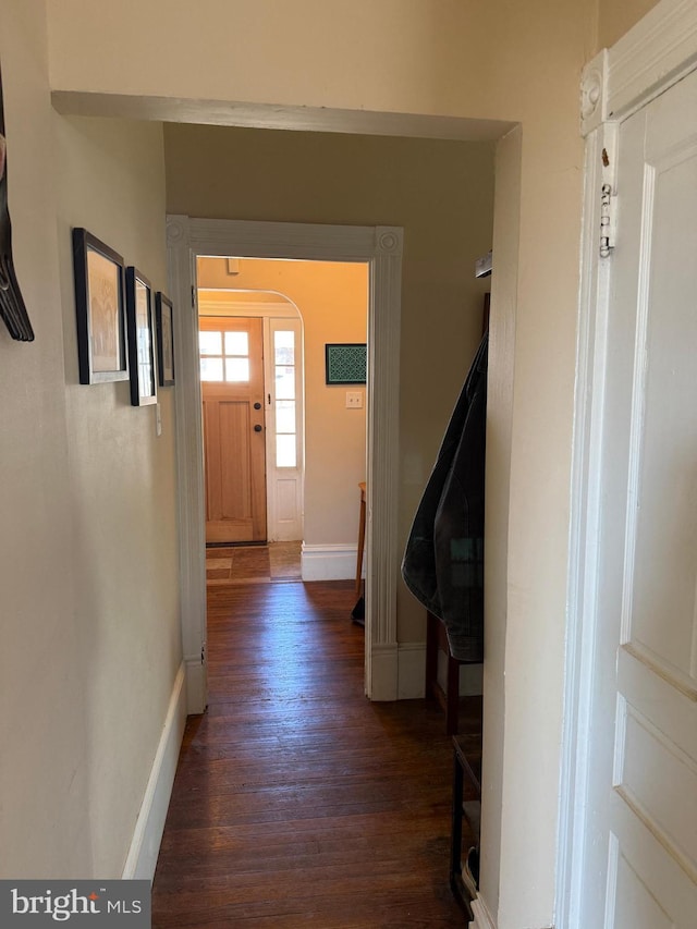 corridor with baseboards, arched walkways, and dark wood-style floors