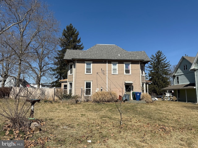 rear view of house featuring a lawn and fence