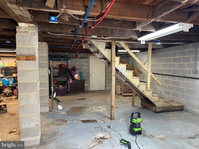 unfinished basement featuring stairway and concrete block wall