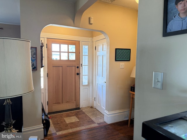 foyer featuring baseboards, arched walkways, and wood finished floors