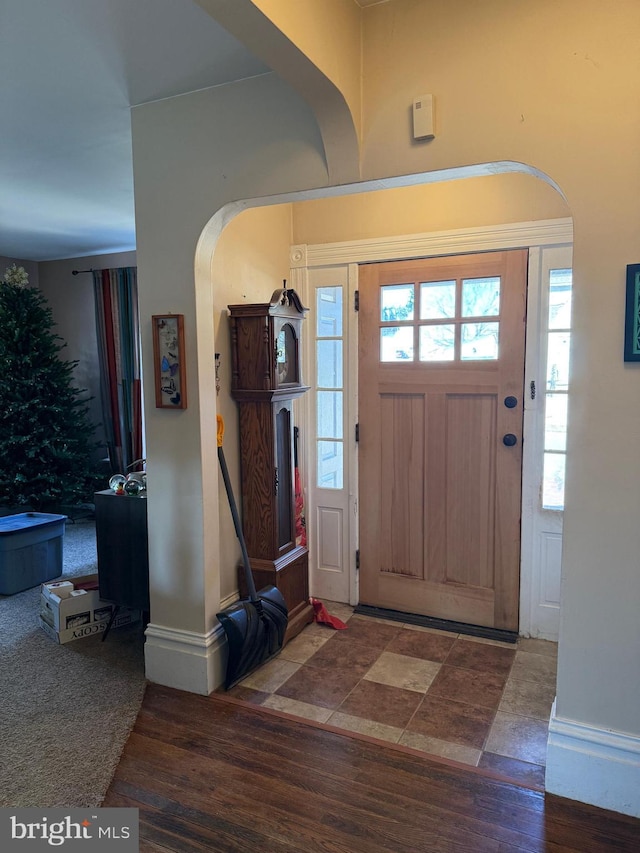 entryway featuring arched walkways, baseboards, and wood finished floors