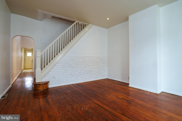 interior space featuring arched walkways, hardwood / wood-style flooring, brick wall, baseboards, and stairway