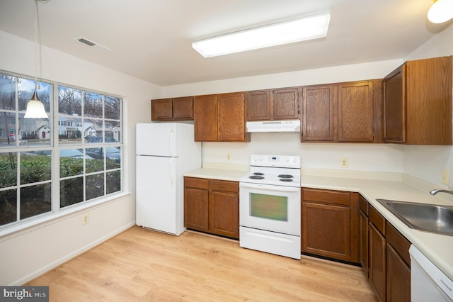 kitchen with white appliances, visible vents, light wood-type flooring, under cabinet range hood, and a sink