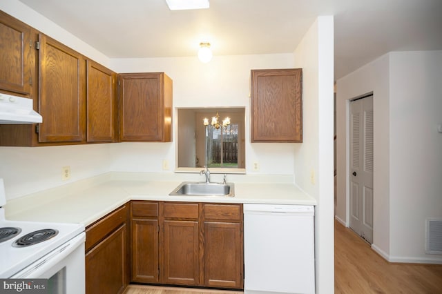 kitchen with white appliances, brown cabinets, light countertops, under cabinet range hood, and a sink