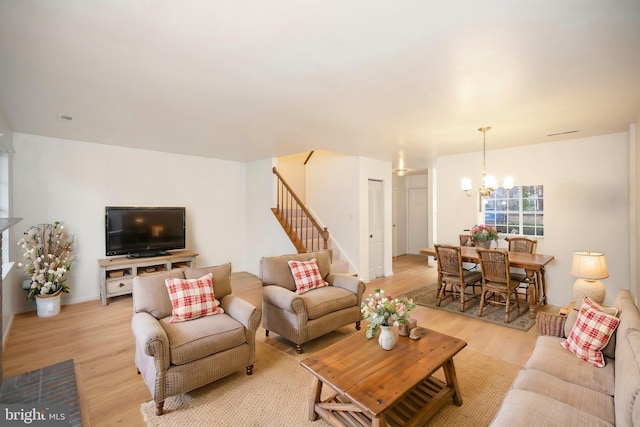 living room featuring an inviting chandelier, light wood-style flooring, visible vents, and stairway